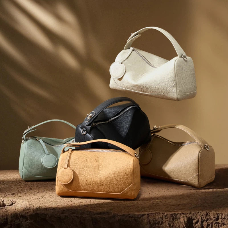 Five Cuirae top grain cowhide handbags in different colors stacked together on a stone surface.
