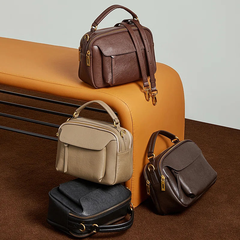 Four Cuirae top grain cowhide shoulder bags in black and brown colors resting around an orange bench.