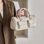 Woman holding Cuirae off white genuine leather barrel bag, closeup showing double front pockets and antique gold hardware
