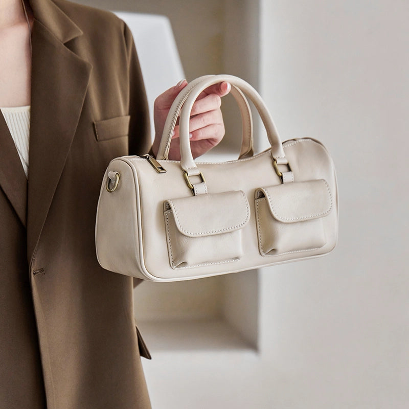 Woman holding Cuirae off white genuine leather barrel bag, closeup showing double front pockets and antique gold hardware