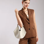 Model wearing Cuirae off-white pebbled leather hobo bucket bag on shoulder, front view with brown blazer outfit