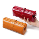 Cuirae red and brown glossy genuine leather makeup bags, one held by hand and one on table, two color variants on white background