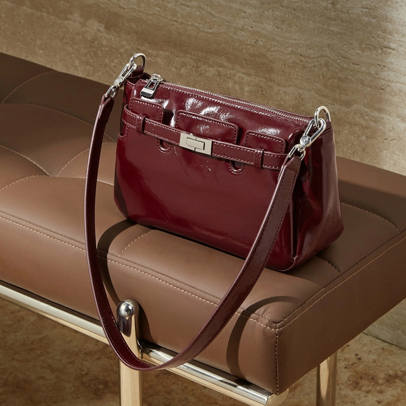 Cuirae red glossy genuine leather crossbody bag on leather bench, showing turnlock detail and adjustable strap
