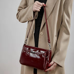 Model holding Cuirae red glossy leather crossbody bag, front view showcasing turnlock detail and sleek texture