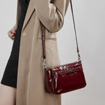 Cuirae red glossy turnlock crossbody bag worn crossbody by model, showing adjustable strap and polished finish