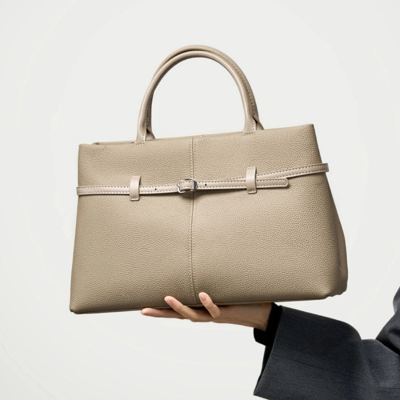 Cuirae taupe genuine leather handbag held in hand, closeup showing pebbled texture and silver belt buckle hardware