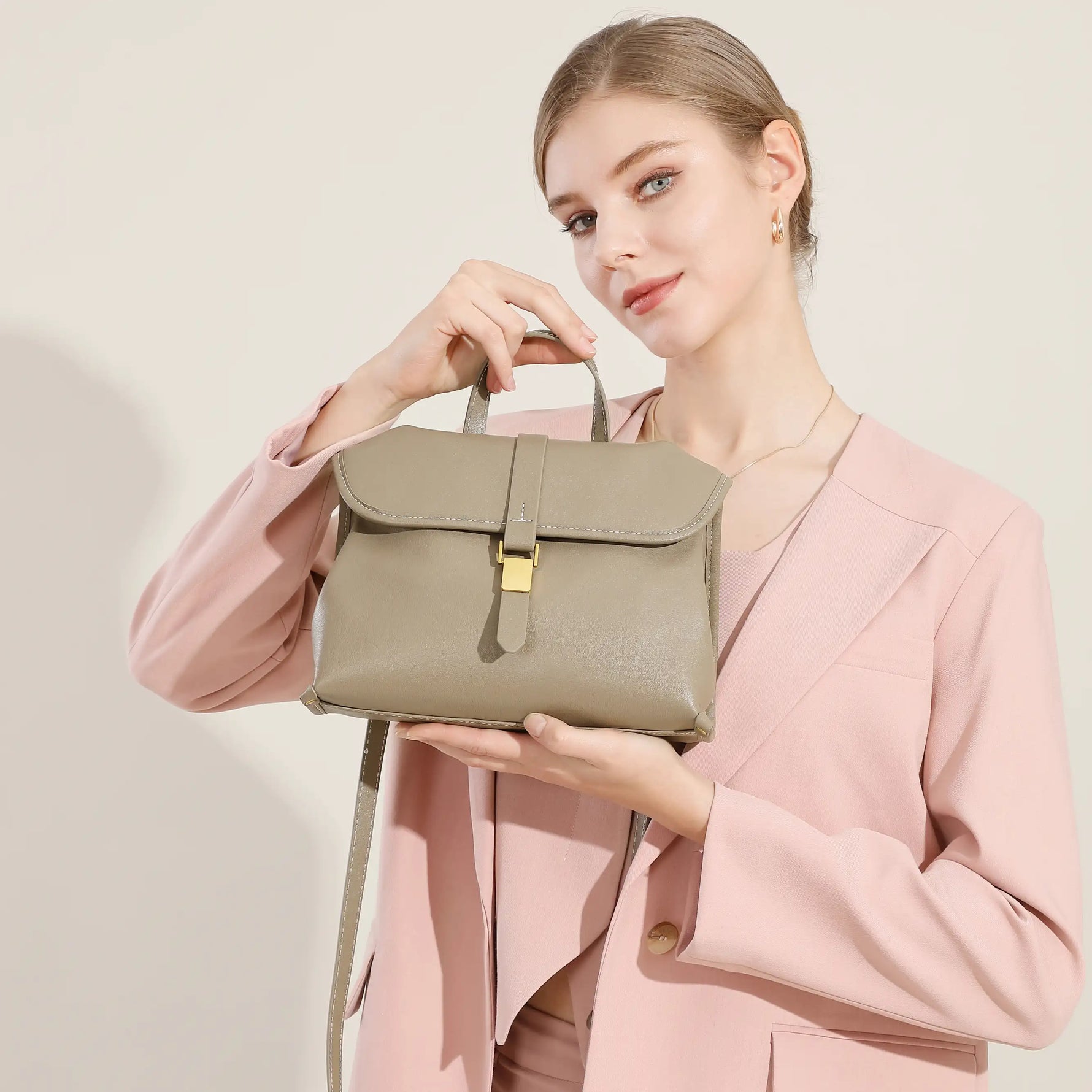 Model holding Cuirae taupe genuine leather handbag with gold buckle, front view showing structured flap design