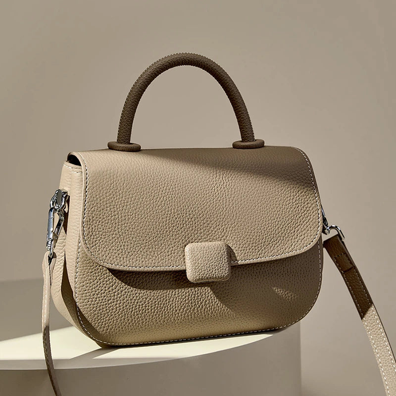 A Cuirae taupe genuine leather shoulder bag with a distinct two-tone handle displayed on a pedestal.