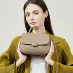 Woman holding Cuirae taupe genuine leather shoulder bag, front closeup showing contrast stitching