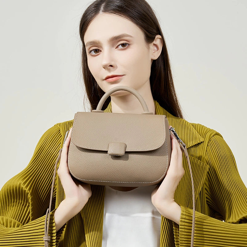 Woman holding Cuirae taupe genuine leather shoulder bag, front closeup showing contrast stitching