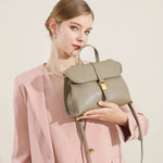 Woman holding Cuirae taupe genuine leather top handle bag, side view showing smooth leather texture