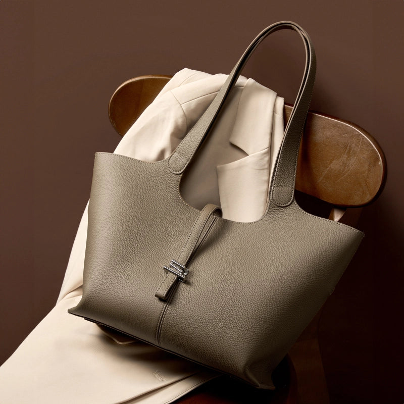 The Cuirae taupe genuine leather tote bag resting on a wooden chair with a light jacket.