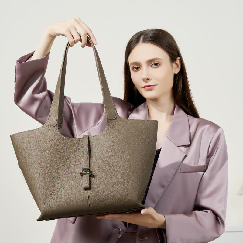 A woman holding the Cuirae taupe genuine leather tote bag to show the front metal clasp.