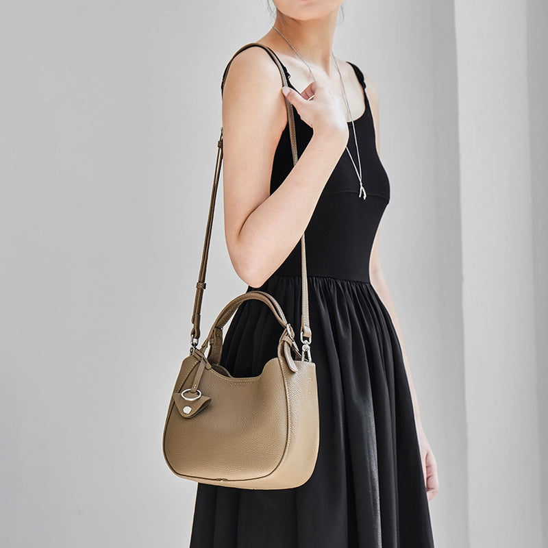 Model wearing Cuirae taupe leather bucket bag on shoulder, front view with hand resting on adjustable strap