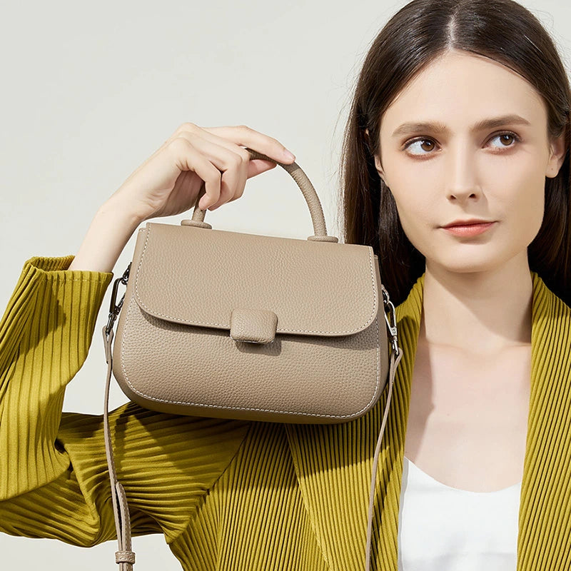 Woman carrying Cuirae taupe genuine leather mini shoulder bag by top handle, front view