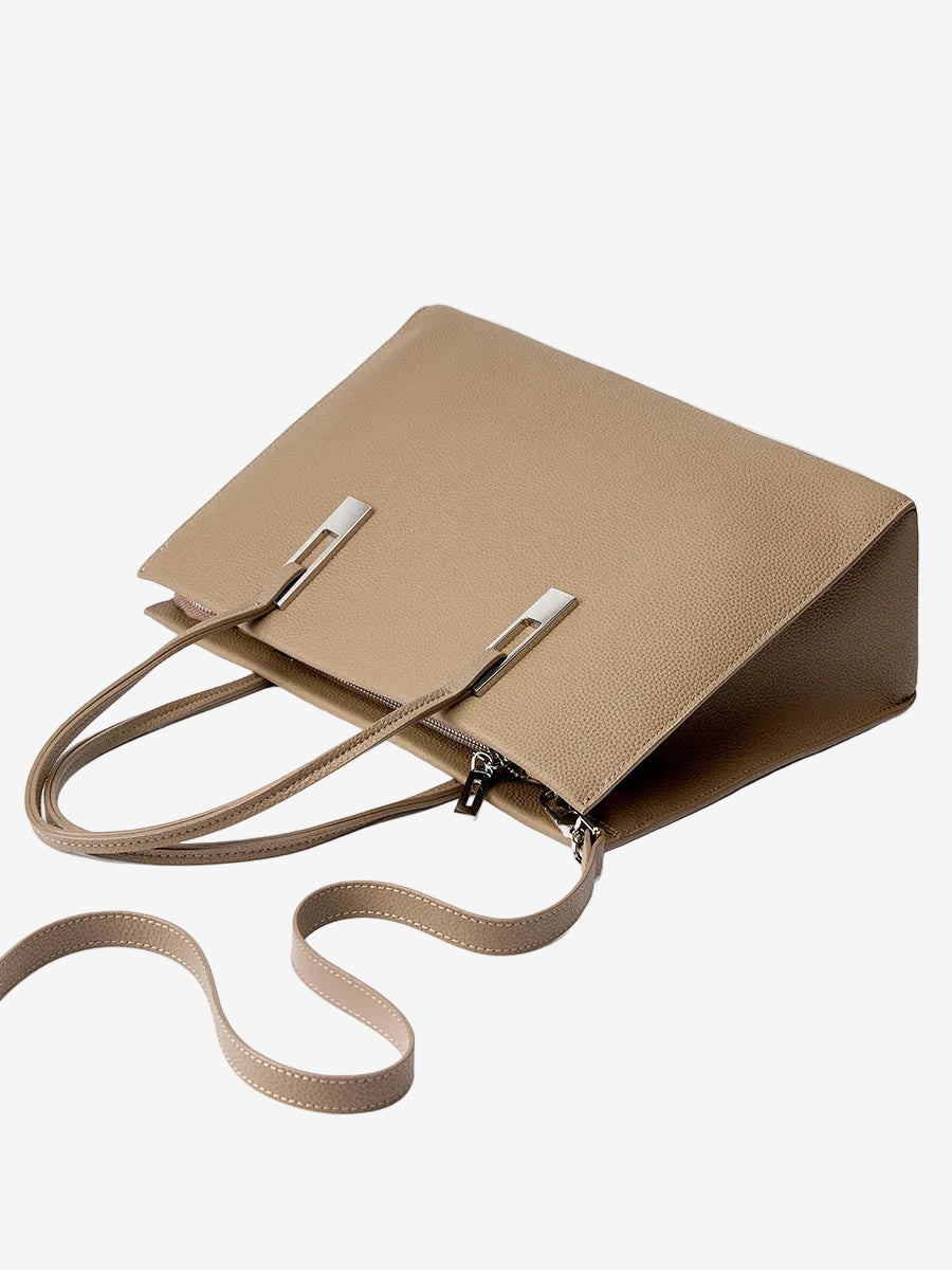 Taupe leather tote laid on its side with its detachable shoulder strap attached