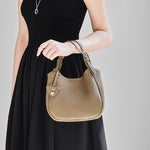 Cuirae taupe pebbled leather bucket bag hanging from model's wrist, front view with black sleeveless dress