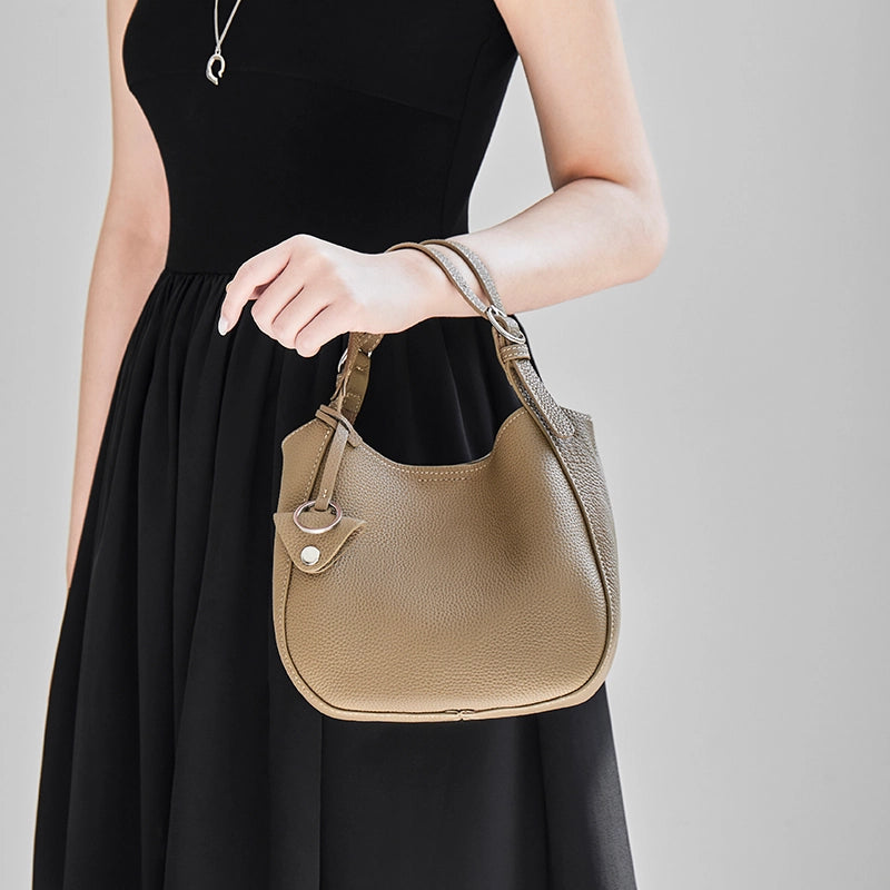 Cuirae taupe pebbled leather bucket bag hanging from model's wrist, front view with black sleeveless dress