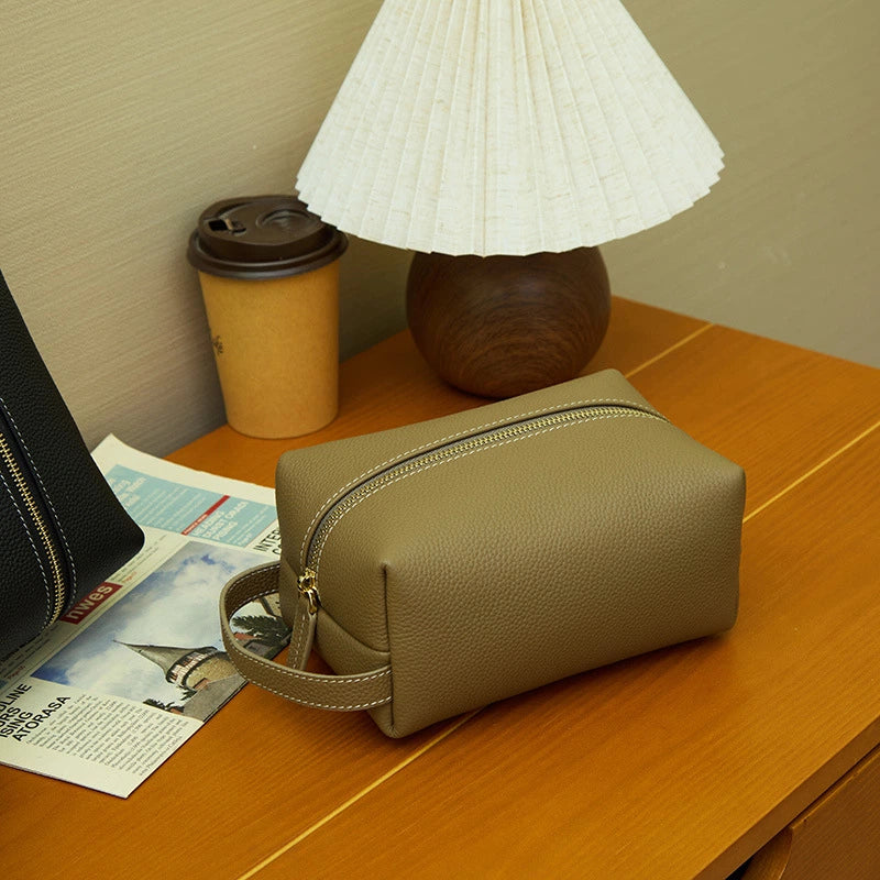 Cuirae taupe pebbled leather makeup bag on wooden nightstand, still life with coffee cup and table lamp
