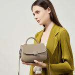 Model holding Cuirae taupe pebbled genuine leather shoulder bag, side view showing detachable shoulder strap