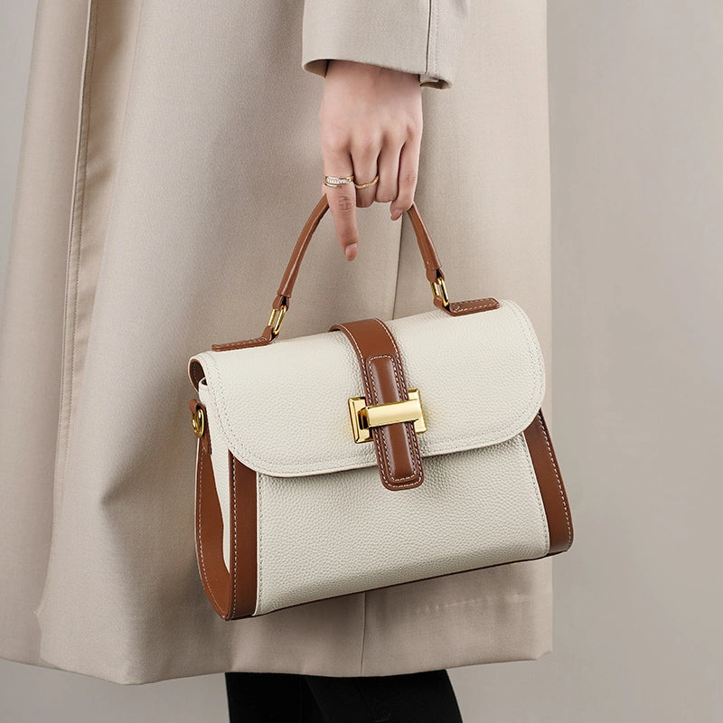 Woman holding Cuirae two tone genuine leather shoulder bag by top handle, front view showing gold turnlock hardware