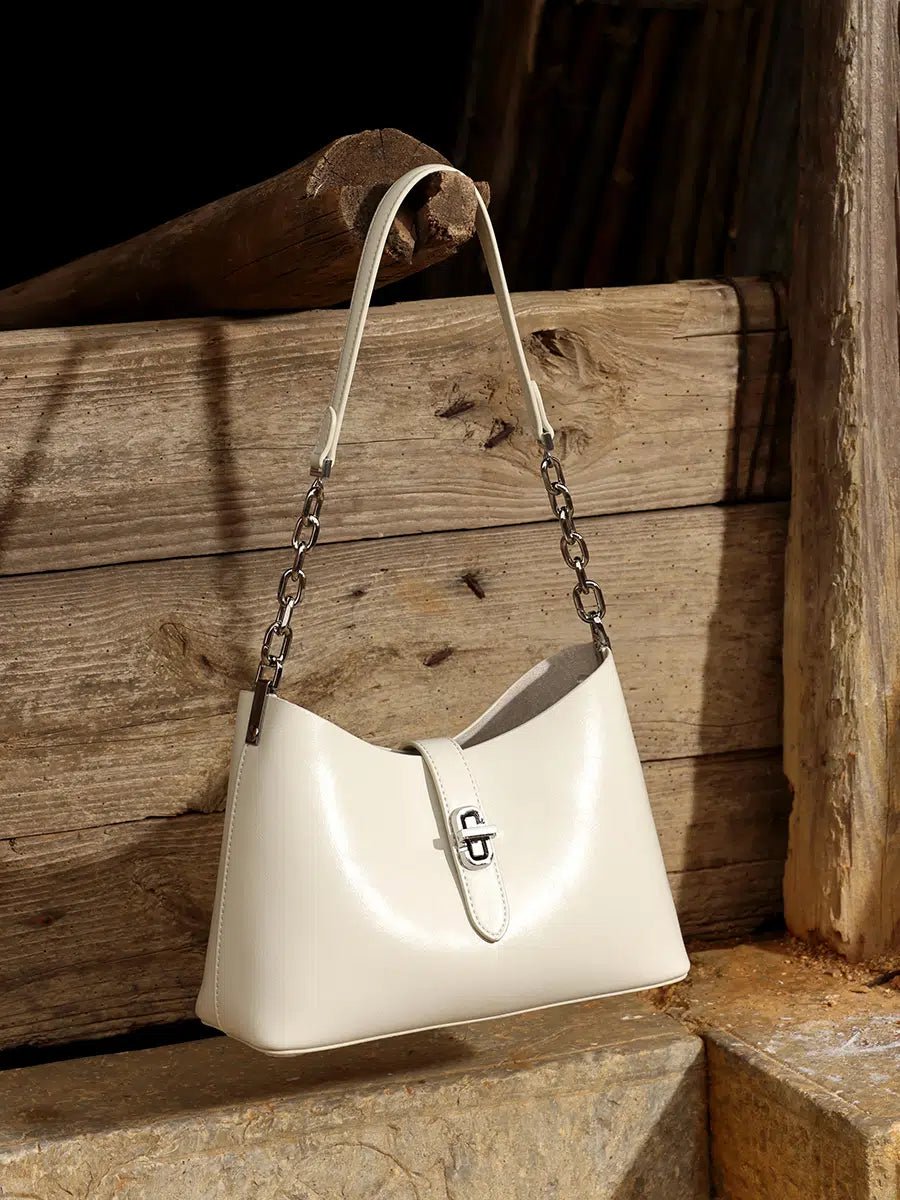 A Cuirae white genuine leather handbag with a chain strap hanging on a wooden fence.