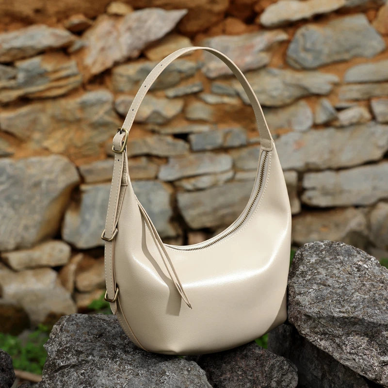 A Cuirae white genuine leather handbag with an adjustable strap resting on a stone wall.