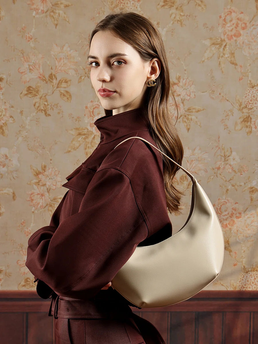 A woman in a dark red outfit wearing the Cuirae white top grain cowhide handbag, standing in front of floral wallpaper.