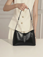 A video of a woman showing the Cuirae black genuine leather handbag. She shows the silver lock, the chain strap, and the inside of the bag.