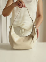 A video showing the Cuirae white genuine leather handbag. A woman presses the soft leather, opens the bag to show the inside, and wears it on her shoulder with a dark red outfit.