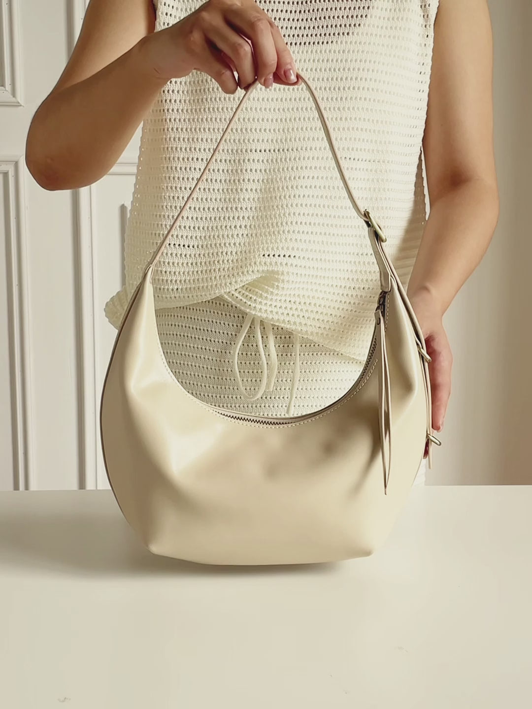 A video showing the Cuirae white genuine leather handbag. A woman presses the soft leather, opens the bag to show the inside, and wears it on her shoulder with a dark red outfit.